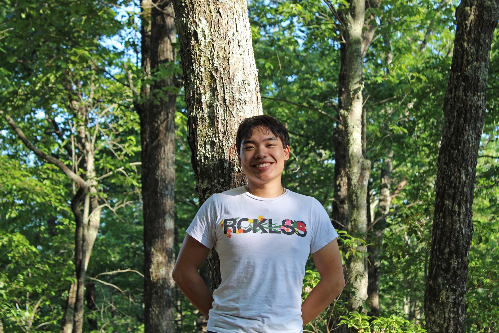 Joshua Tan standing under a tree in a forest.