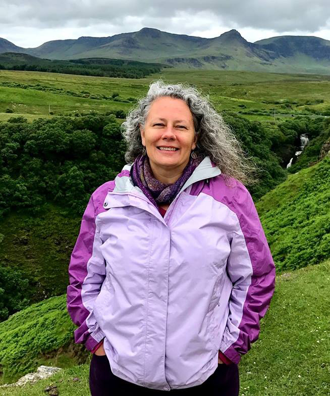 A woman wearing a purple rain jacket with a lush, natural green background