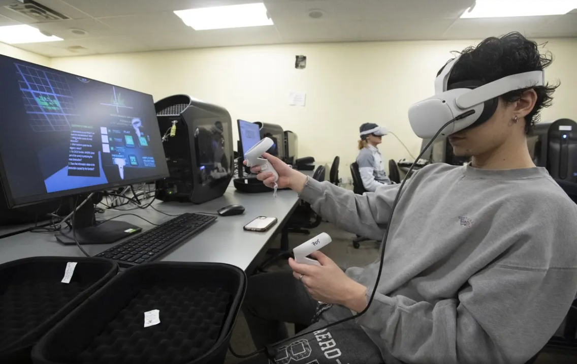 A student sits at a desk with a virtual reality headset on