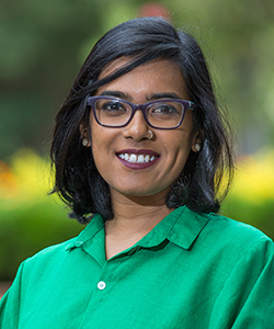 A woman smiling wearing a green blouse with glasses.