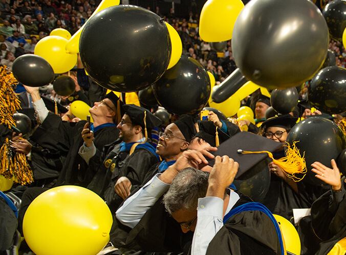 Students celebrate graduation as black and gold baloons are released into the air.